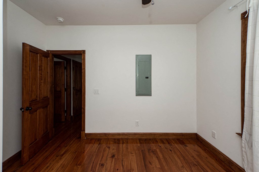 A room with a wooden floor and a white wall with a door and a cupboard.