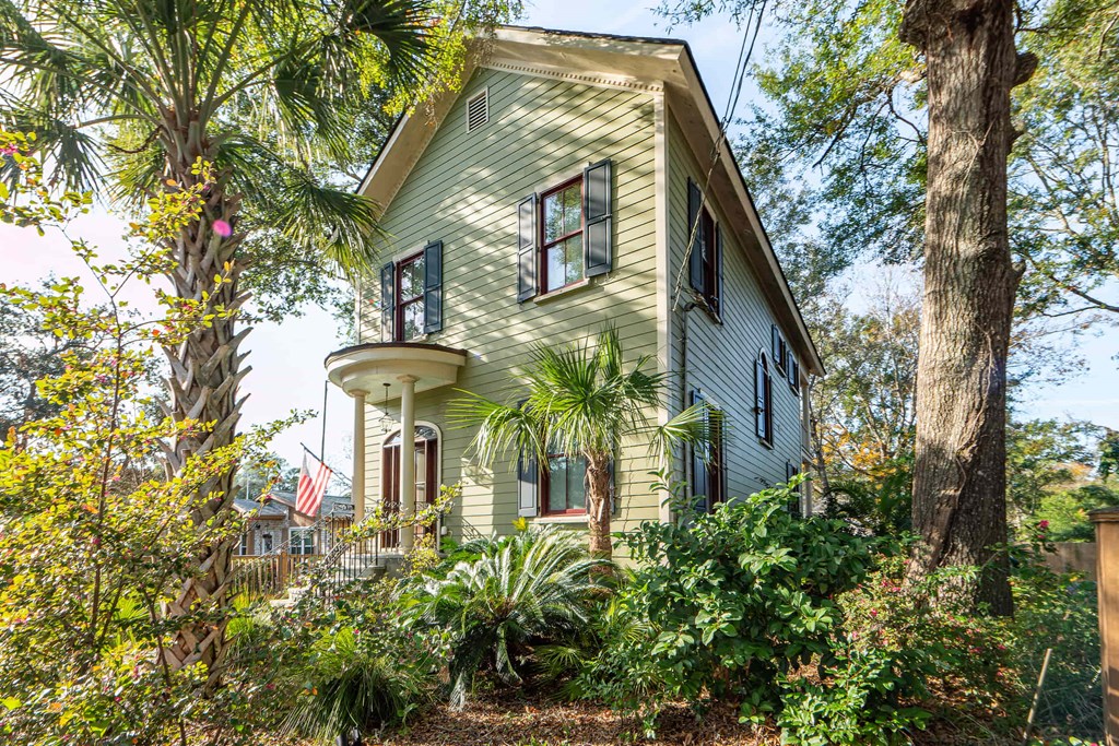 A house with a greenish exterior surrounded by trees and plants.