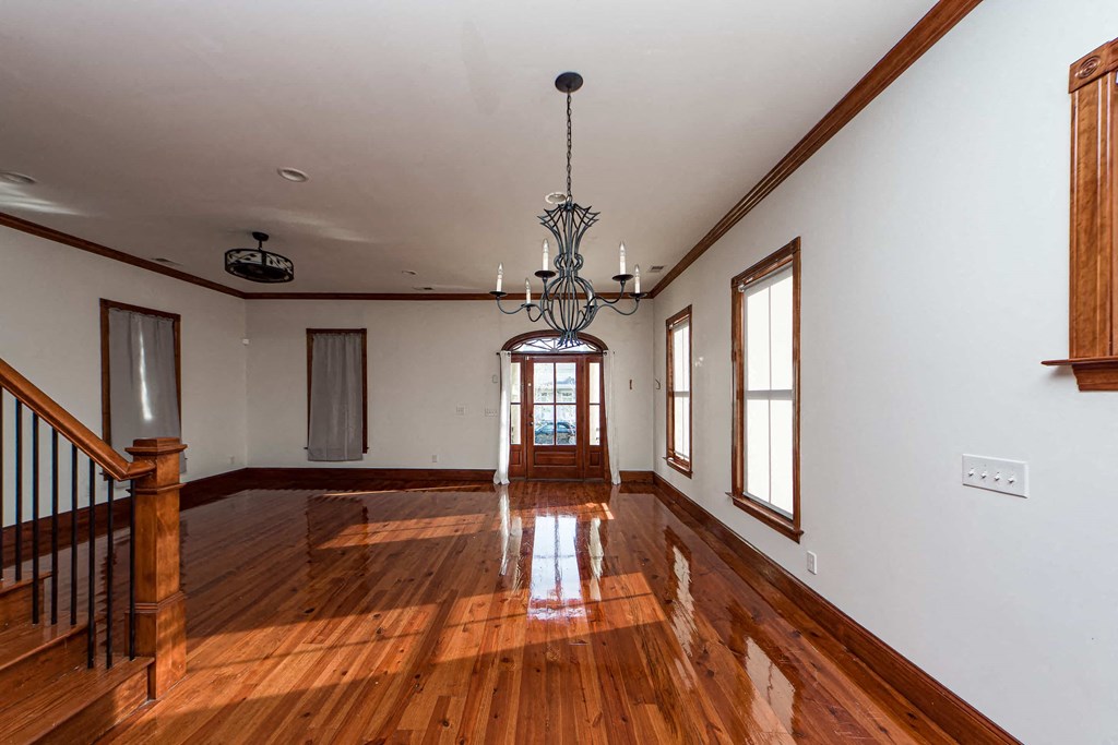 A large, empty room with wooden floors and a chandelier hanging from the ceiling.