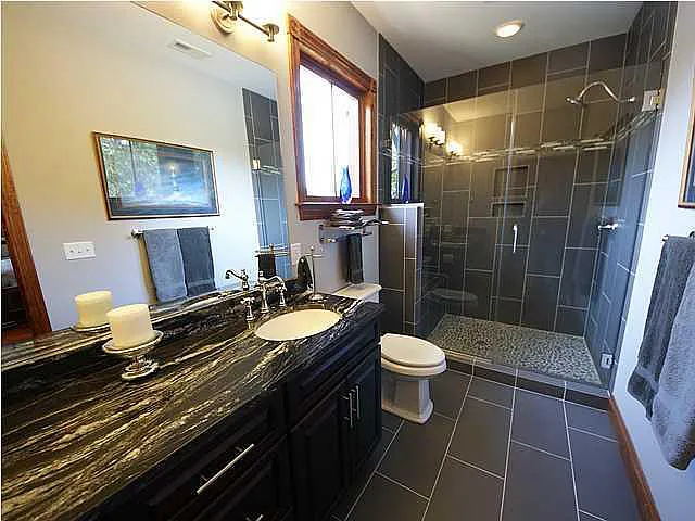 A bathroom with a black granite counter top and a walk in shower.