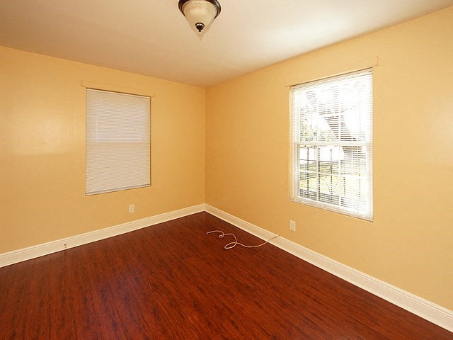 an empty room with a wood floor and two windows