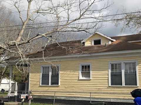 A yellow house with a brown roof and a tree in front.