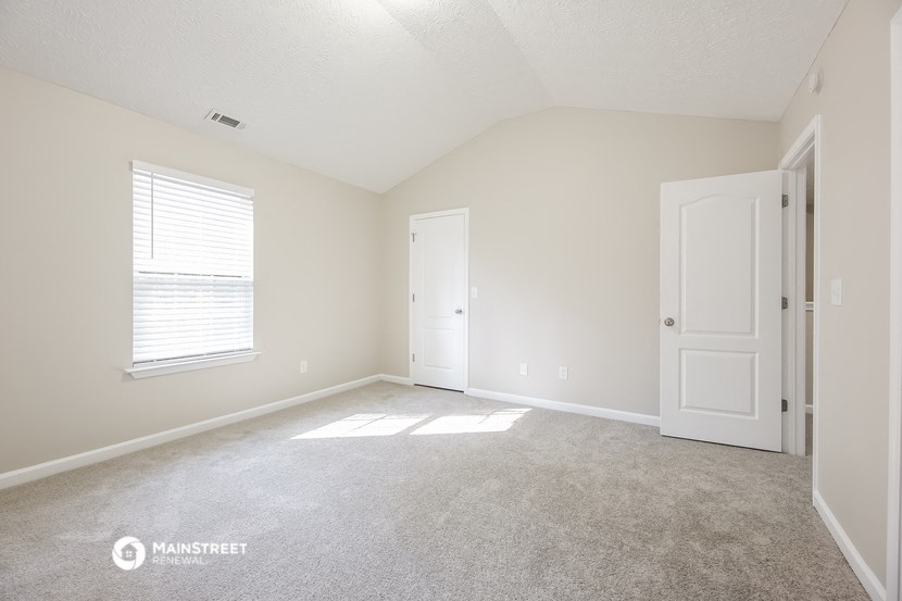 a bedroom with white walls and carpet and a white door and window