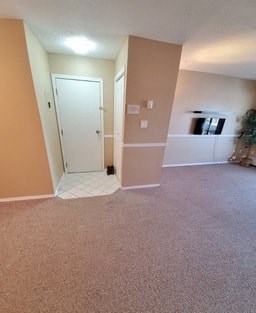 an empty carpeted living room with a door to a hallway