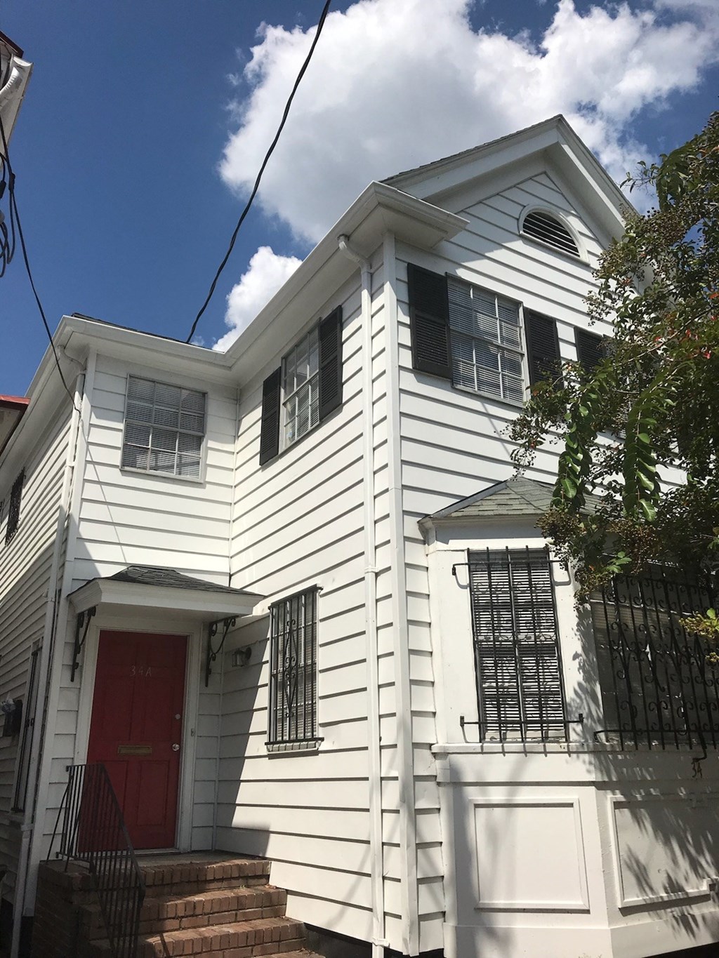 A white house with a red door and a balcony with a railing.
