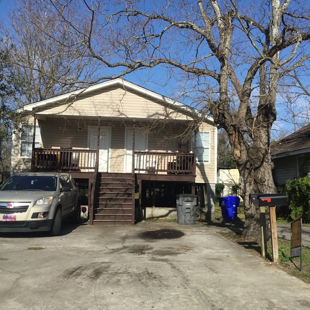 A silver car is parked in front of a two-story house.