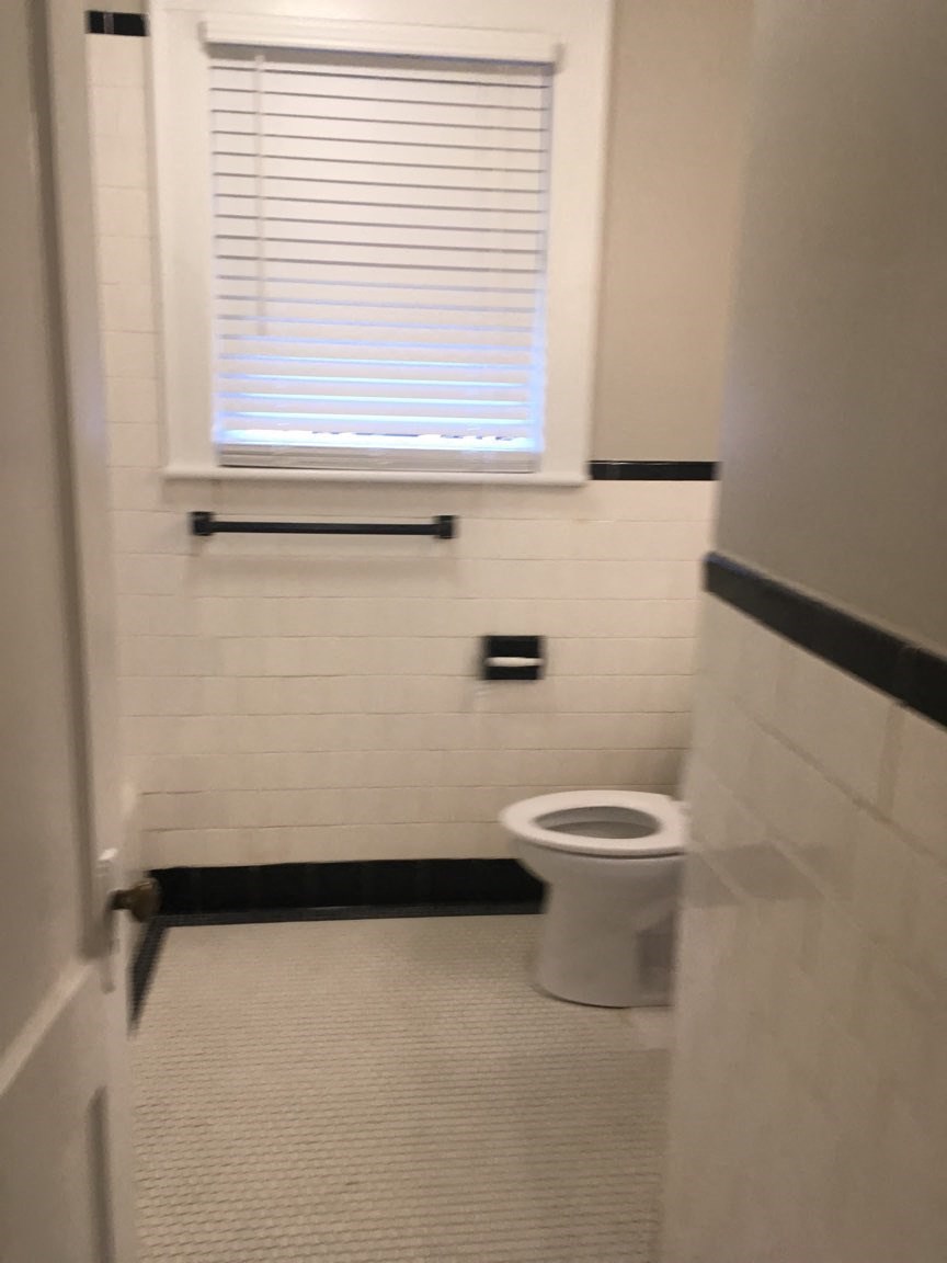 A white toilet in a bathroom with a window above it.