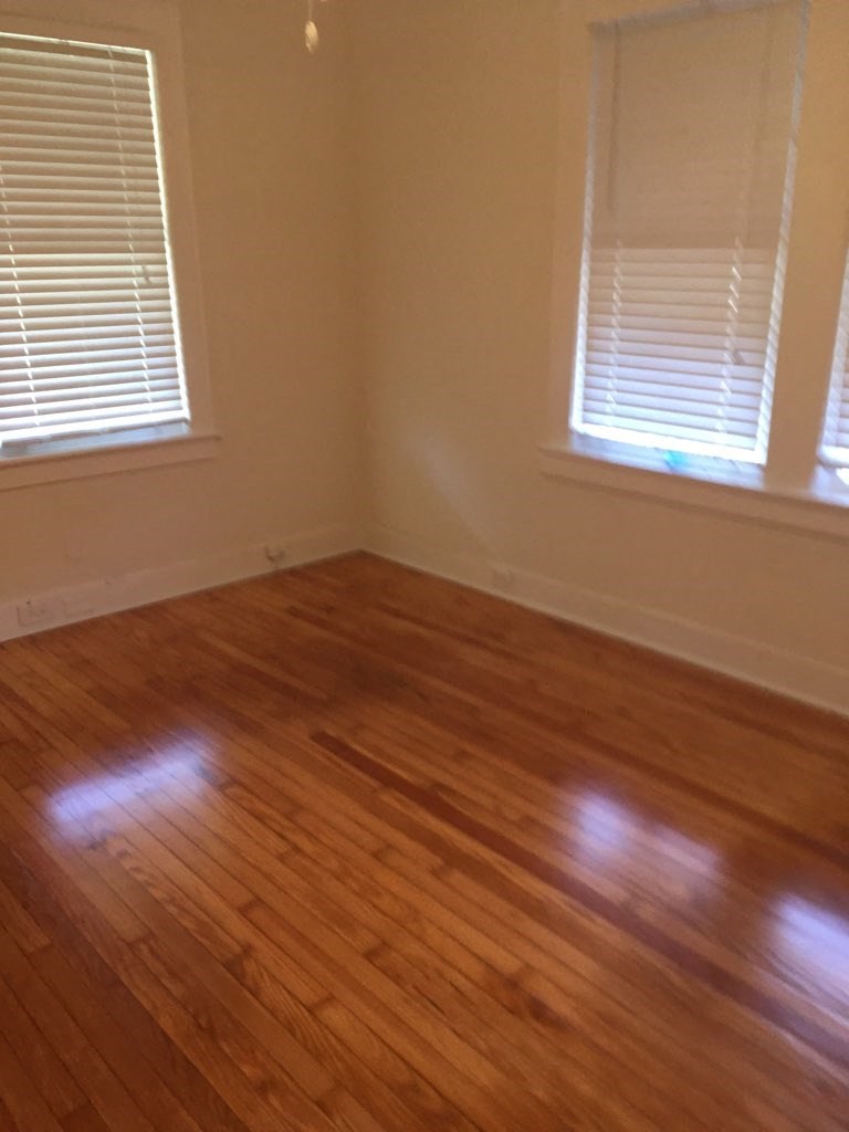 A room with wooden floors and two windows with blinds.