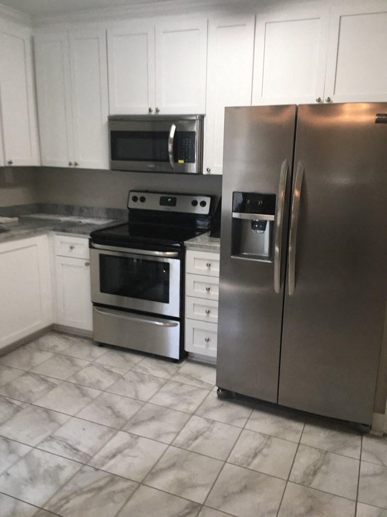 A kitchen with a stove, oven, refrigerator, microwave and cabinets.