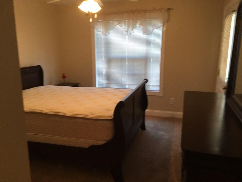 A bedroom with a bed, dresser, and window with blinds.