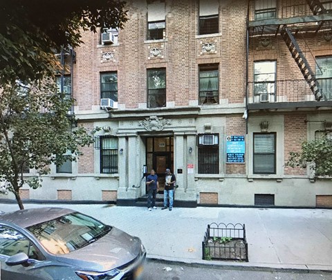 A silver car is parked on the side of the street in front of a building.