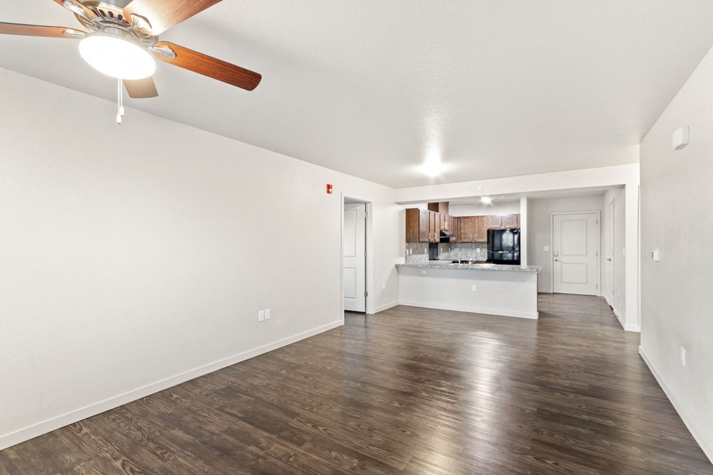 an empty living room with a ceiling fan and a kitchen