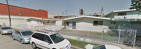 A white car is parked in front of a white building with a red roof.