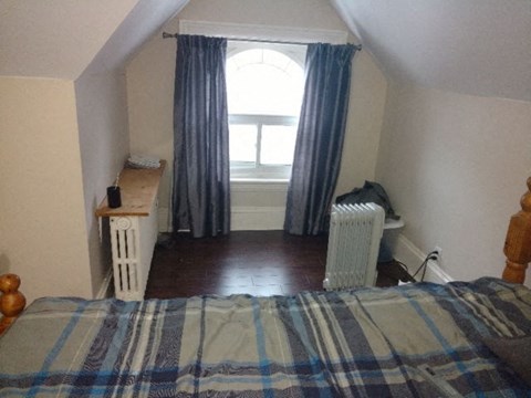 A bedroom with a bed, a radiator, and a window with curtains.