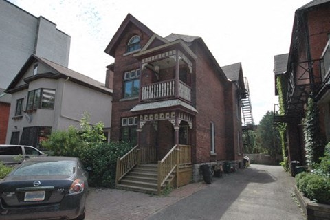 A car is parked in front of a brick building with a balcony.