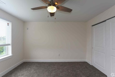 an empty bedroom with a ceiling fan and a window