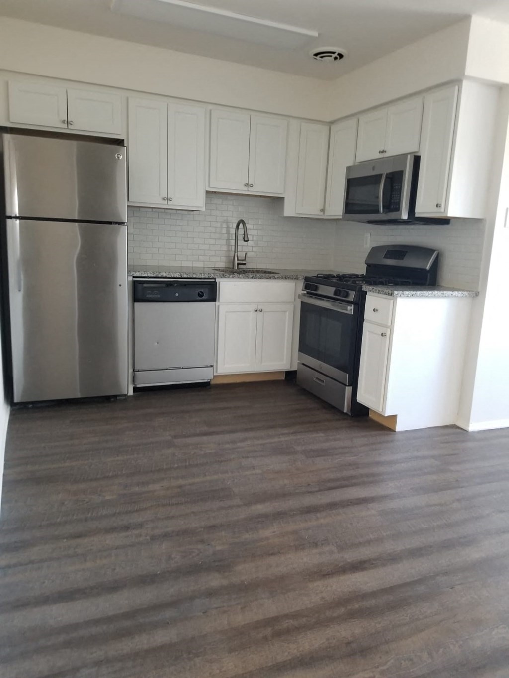an empty kitchen with stainless steel appliances and white cabinets
