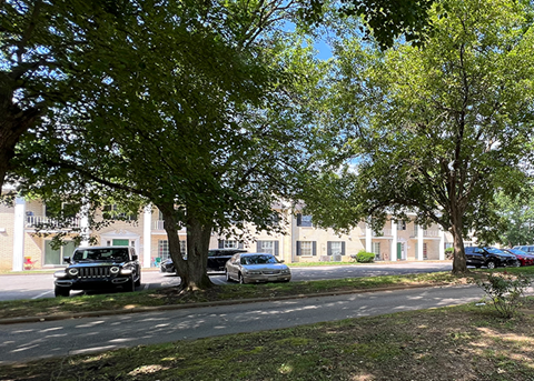 Front view of an apartment complex with shaded parking area and mature trees
