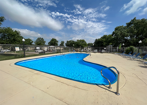 Outdoor swimming pool with clear blue water, surrounded by lounge chairs and fencing under a sunny sky.