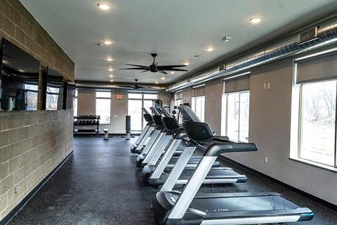a gym with cardio machines and a ceiling fan