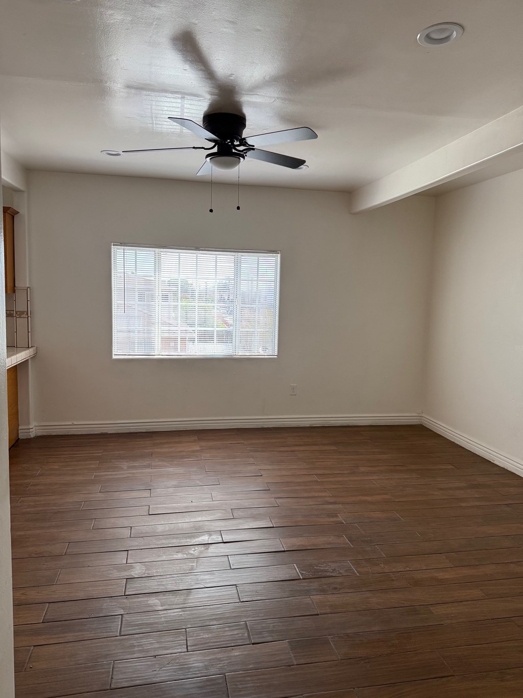 A room with a ceiling fan and a window with blinds.