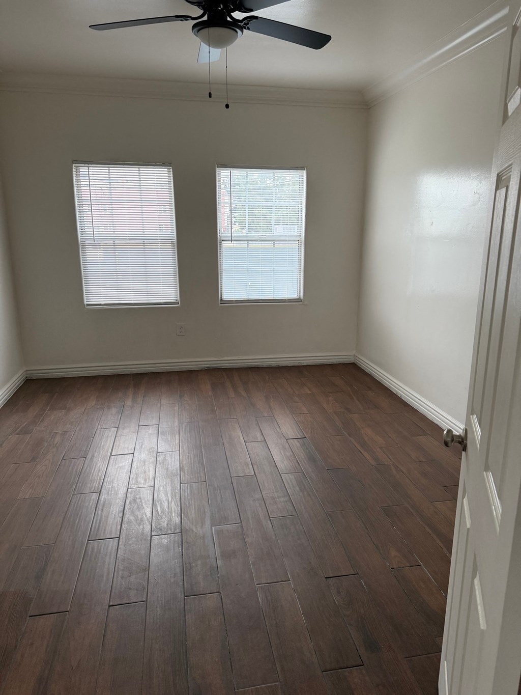 A room with a ceiling fan and two windows.