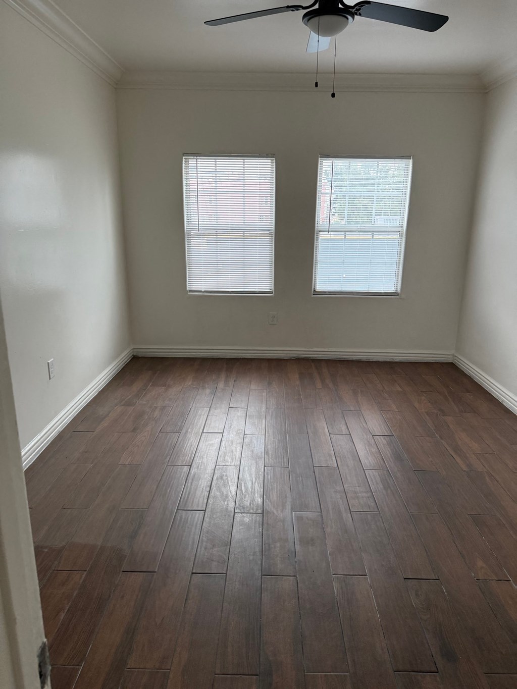 A room with a ceiling fan and two windows.