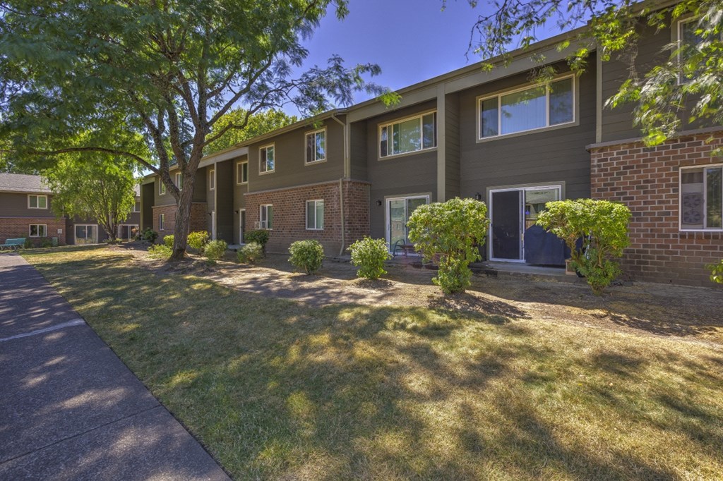 an apartment building with a lawn and trees in front of it