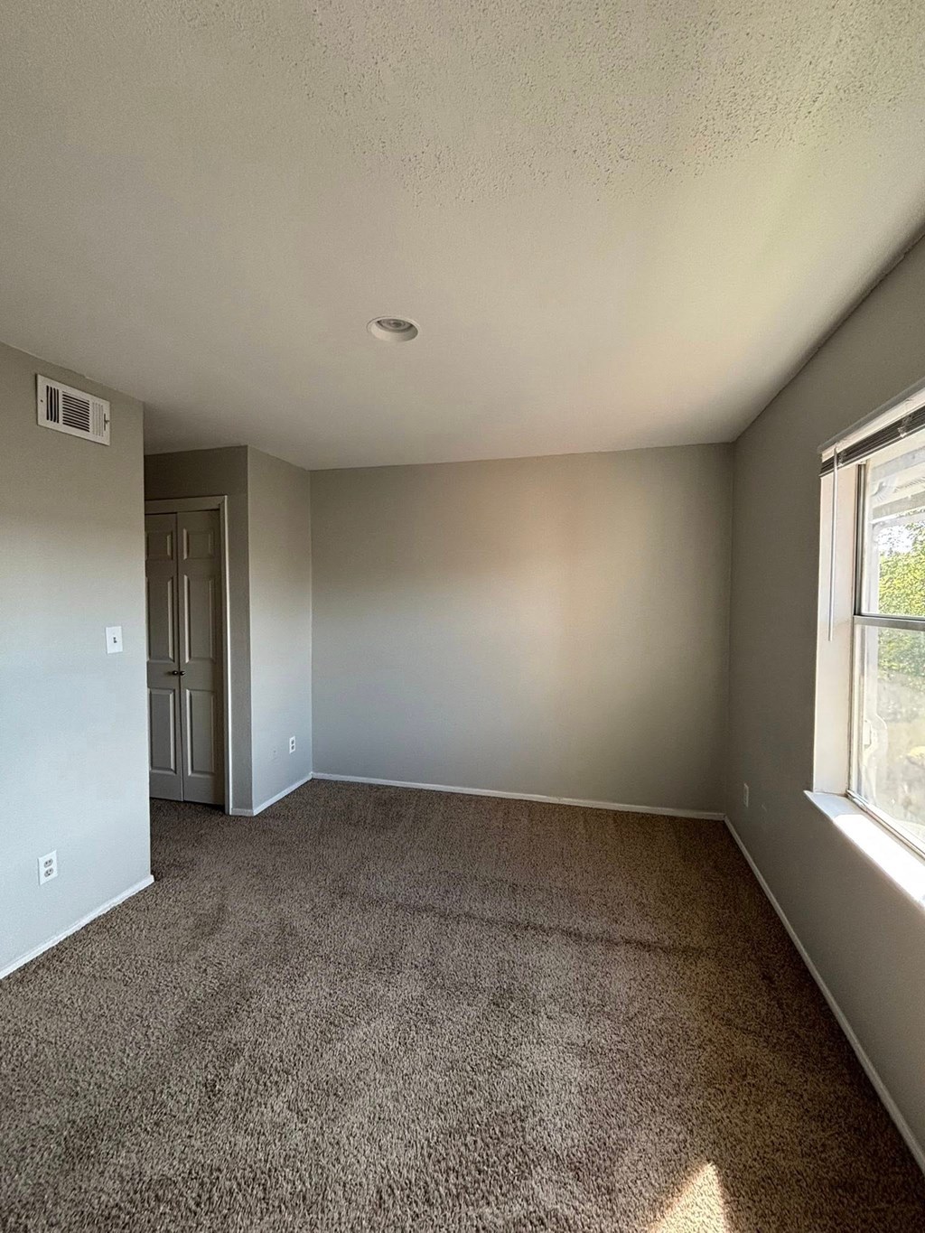 A room with a carpeted floor and a window letting in sunlight.