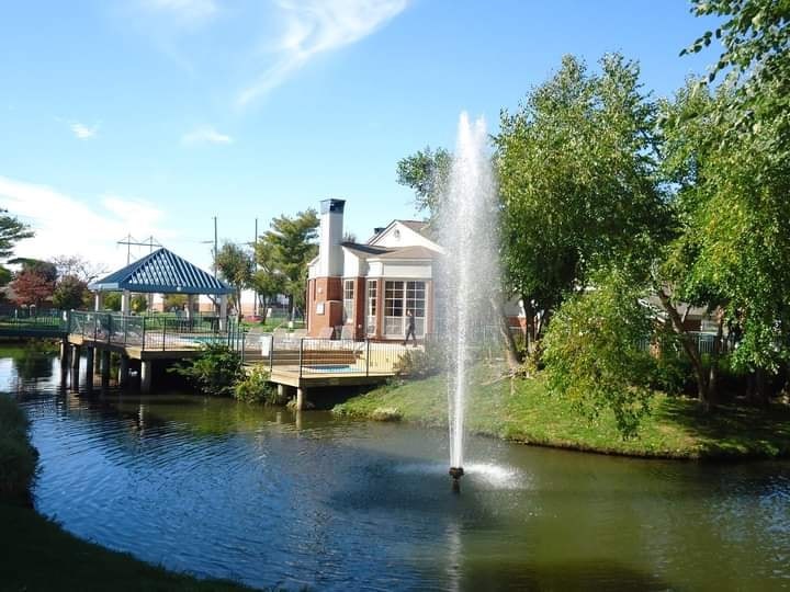 A fountain in the middle of a pond in front of a building.