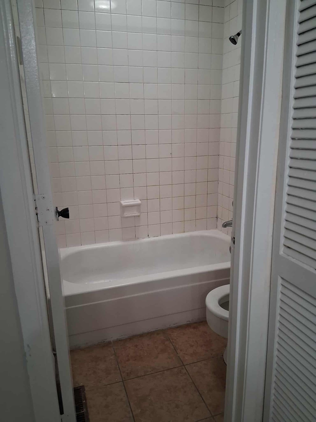 A white tiled bathroom with a toilet and tub.