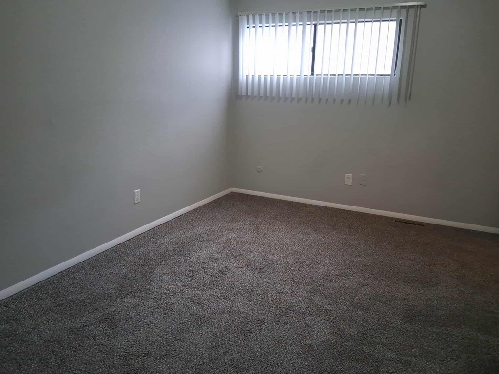 A room with a carpeted floor and a window with blinds.