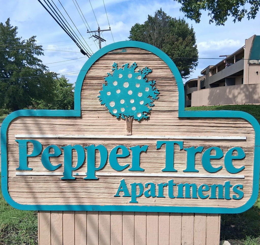A sign for Pepper Tree Apartments with a blue background and a tree design.