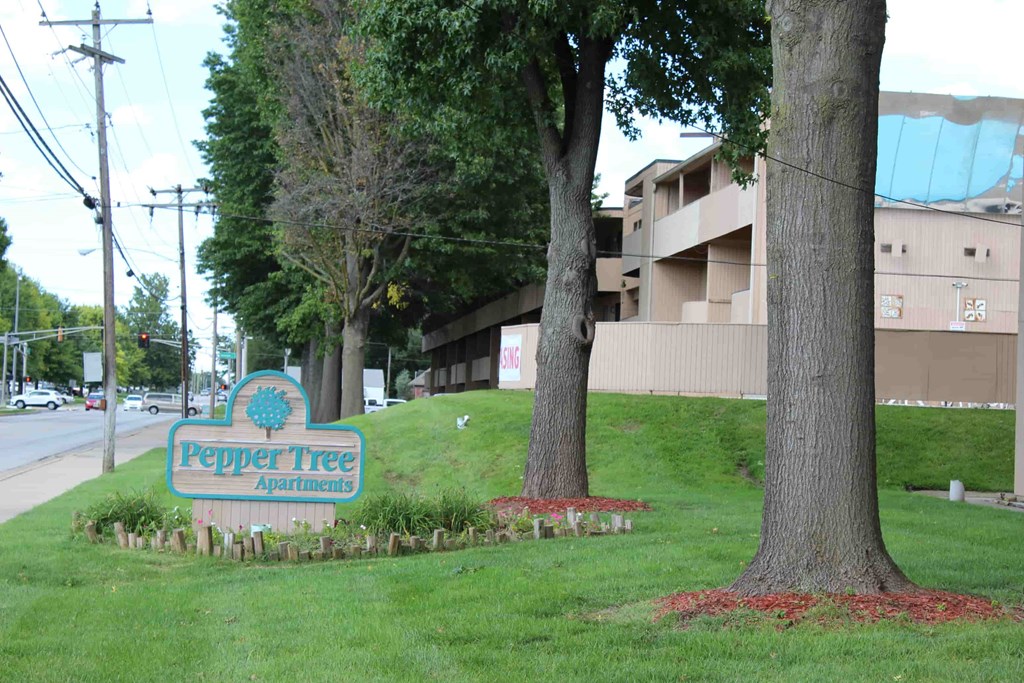 A sign for Pepper Tree Apartments is in front of a grassy area.