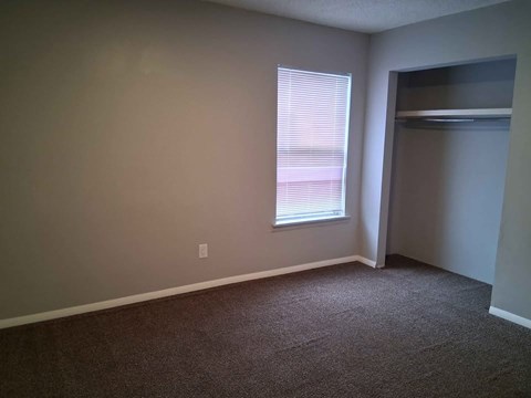 A room with a carpeted floor and a window with blinds.