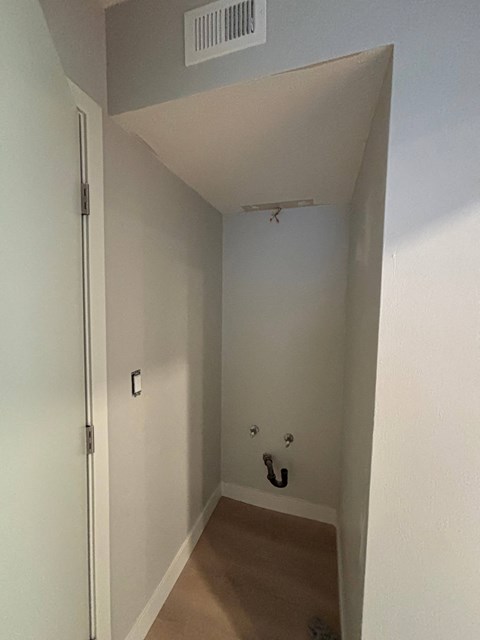 A white door with a silver handle is on the left side of a hallway with a light switch and a black hook on the wall.