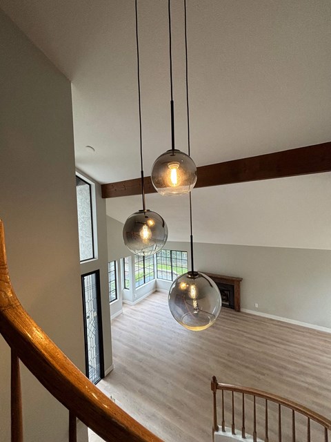 Three spherical pendant lights are suspended from the ceiling in a spacious room with a wooden staircase.