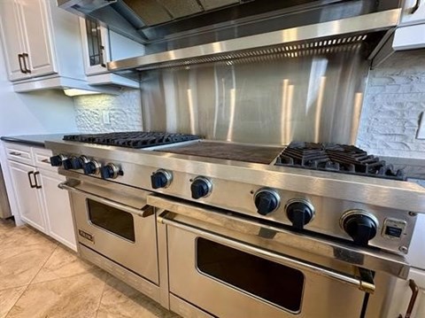 A stainless steel gas range with four burners and two ovens in a kitchen.