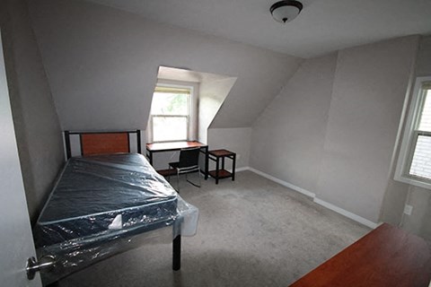 A bedroom with a bed, desk, and window.