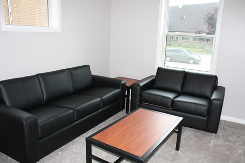 A black leather sofa and loveseat with a wooden coffee table in a room with a window.