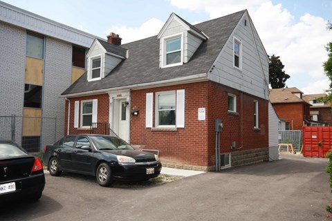 A black car is parked in front of a brick house.