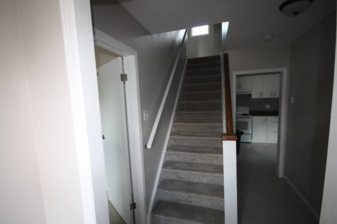 A staircase with a white railing leads to a kitchen area.