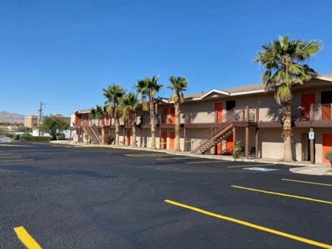 A parking lot with a building and palm trees in the background.