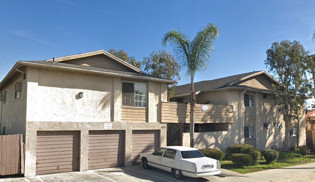 A white car is parked in front of a house with a brown garage door.