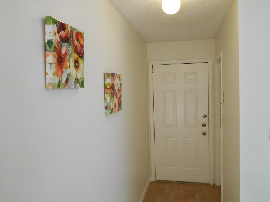 A hallway with a white door and two pictures on the wall.
