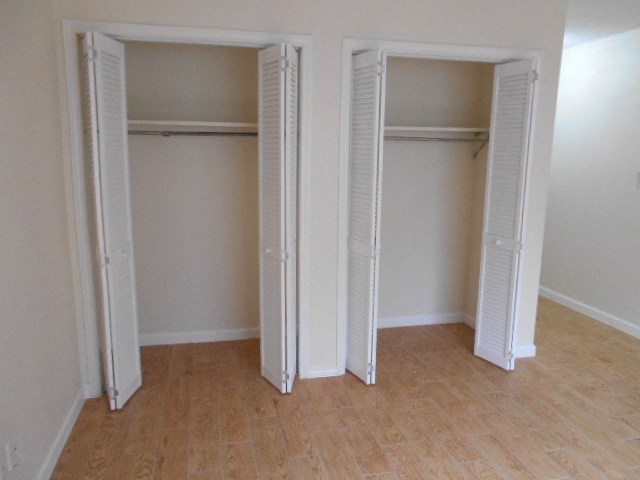 Three white closet doors are open in a room with wood floors.