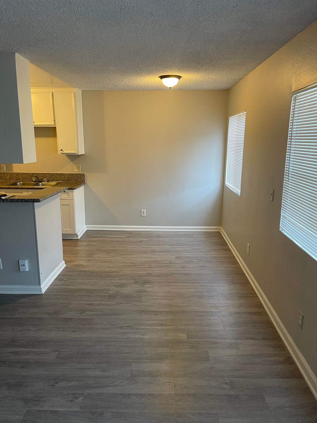 an empty living room with wood floors and a kitchen