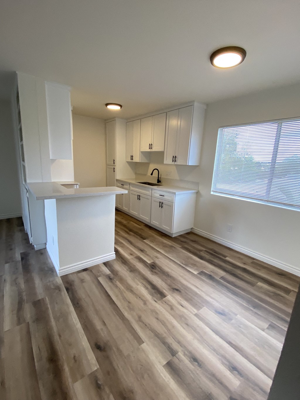 an empty kitchen with wooden floors and white cabinets