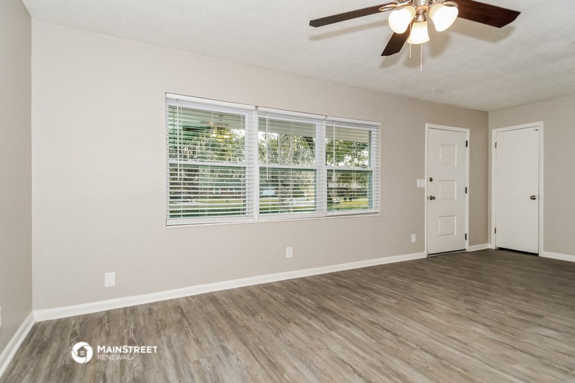 the spacious living room with a large window and a ceiling fan