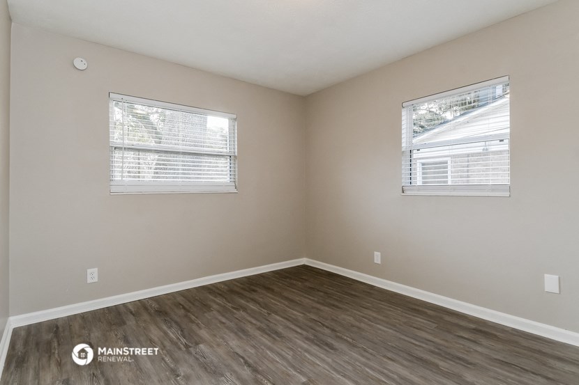 the interior of a bedroom with wood flooring and two windows